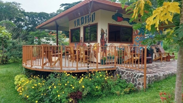 A building with a covered patio area, surrounded by lush greenery and yellow flowers. - Peaceful campground in Monteverde perfect for nature lovers (San Luis de Monteverde)
