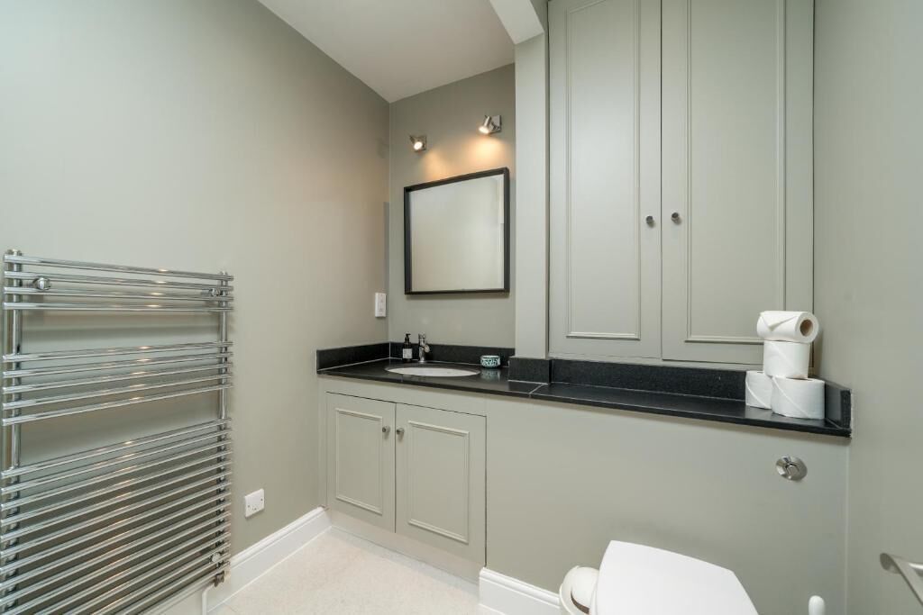 A bathroom with a toilet, sink, and mirror. There is a towel rack and a toilet paper holder on the counter.
