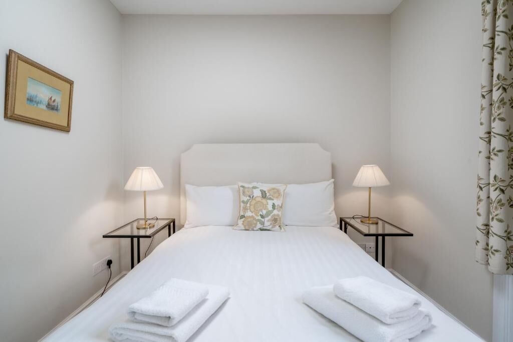 A neatly made bed with white linens and two bedside lamps.