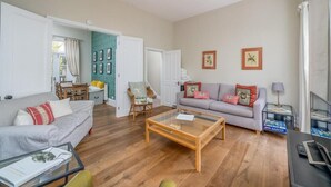 A living room with a sofa, armchair, coffee table, and a TV stand. - Spacious flat near Victoria and Warwick Square (London)