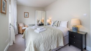 A bedroom with a large bed, a nightstand, a chair, a wardrobe, and a mirror. - Spacious flat near Victoria and Warwick Square (London)