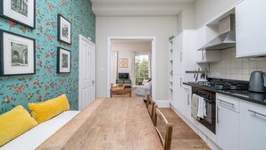 A kitchen with white cabinets, a wooden table, and a floral wallpaper. - Spacious flat near Victoria and Warwick Square (London)