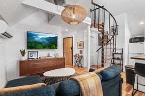 Un salon moderne avec une grande télévision, un meuble en bois, un canapé et un escalier.
