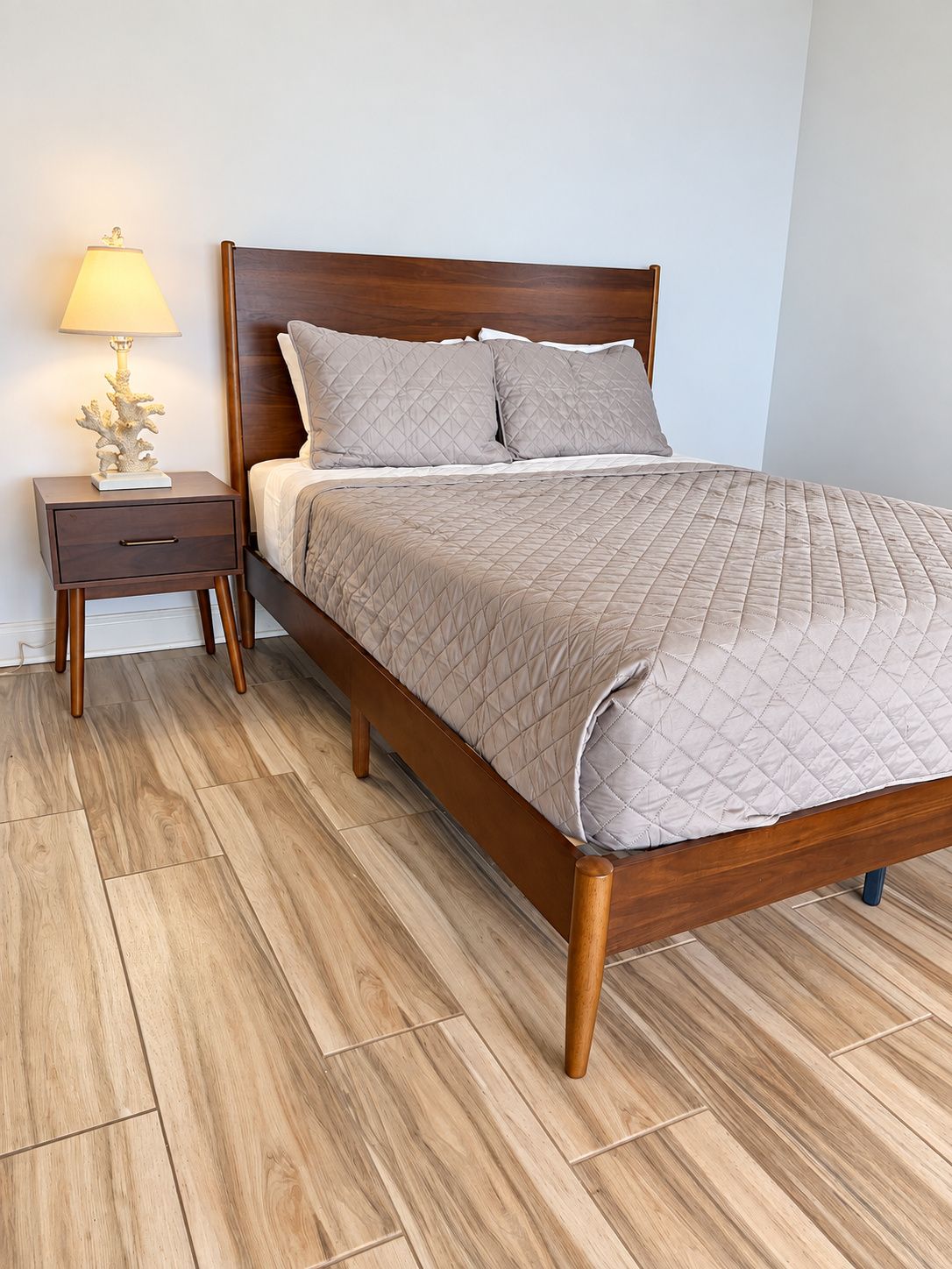 A bed with a wooden frame, a nightstand with a lamp, and a patterned floor.