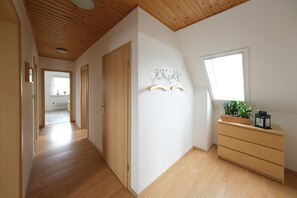A hallway with wooden flooring, a wooden ceiling, a wooden door, a white wall with a window, and a wooden dresser with a plant and a lantern. - Apartment "Barsch" with Balcony and Wi-Fi (Rade)