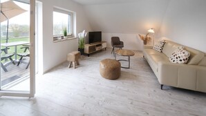 Een ruime woonkamer met een bank, poef, televisie en een eettafel.