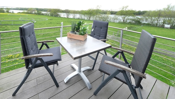 Een terras met tafel en stoelen, met uitzicht op een meer en groene velden.