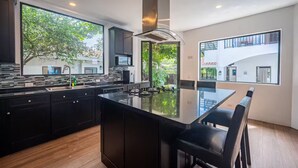 Una cocina moderna con una isla grande, armarios oscuros y ventanas amplias que ofrecen vistas al exterior.