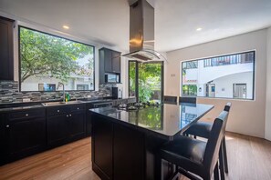 A modern kitchen with a large island, dark cabinetry, and large windows offering views of the outdoors. - BEACH FRONT VILLA 11 Bedrooms Casa Playa Del Rey House (Jaco)