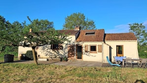 Einbungalow mit Ziegeldach, einer Haustür und einem kleinen Vorbereich mit Tisch und Stühlen.