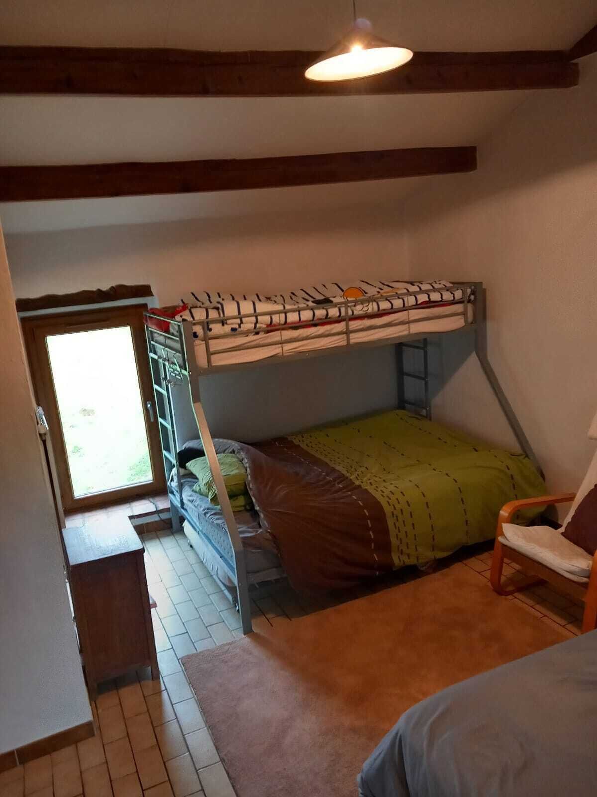 Ein Schlafsaalzimmer mit Etagenbett, Stuhl, kleinem Tisch und Fenster.