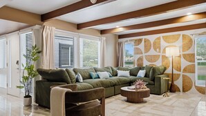 A living room with a sectional sofa, a coffee table, and a lamp. There is a potted plant and a window with blinds. - Fun-Filled Oasis • Pool, Pickleball, Games Galore (Scottsdale)