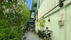 A narrow alleyway with a push button to open a gate, potted plants, and a building with green shutters. - greenteakhouse (Bangkok)