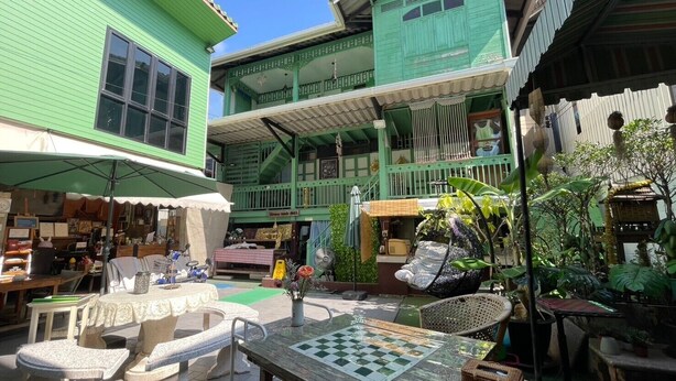 A courtyard with outdoor seating, a chessboard, and a green building with a balcony. - greenteakhouse (Bangkok)