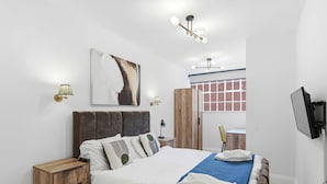 Ein modernes Schlafzimmer mit einem großen Bett, einem Nachttisch aus Holz, einem Schreibtisch und einem Fernseher.