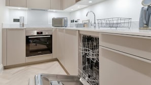Eine moderne Küche mit integrierten Geräten, einem Geschirrspüler und einer Arbeitsplatte mit Spüle und Wasserkocher.
