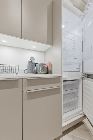 A modern kitchen with white cabinetry, a kettle, a toaster, and a refrigerator with a water dispenser. - 1BED Central Birmingham Flat w Parking & Terrace (Birmingham)
