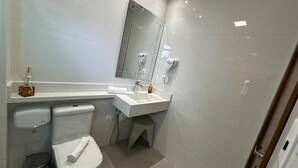 Een moderne badkamer met toilet, wastafel en spiegel. Er is een haardroger aan de muur en een zeepdispenser op het aanrecht.