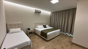 Een hotelkamer met twee eenpersoonsbedden, een tweepersoonsbed, een nachtkastje met lamp en een airconditioning.