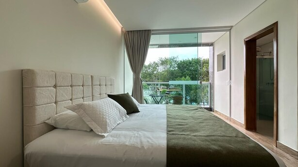 Een moderne slaapkamer met een groot bed, uitzicht op groen en een schuifdeur naar een balkon.