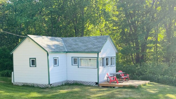 A small, single-story house with a sloped roof, a front porch, and a deck with red chairs.
