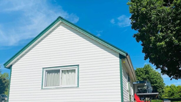 Una casa blanca de un piso con techo verde, una ventana pequeña y una silla roja afuera.