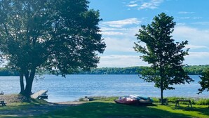 A lakeside setting with trees, a dock, a picnic table, and a canoe.