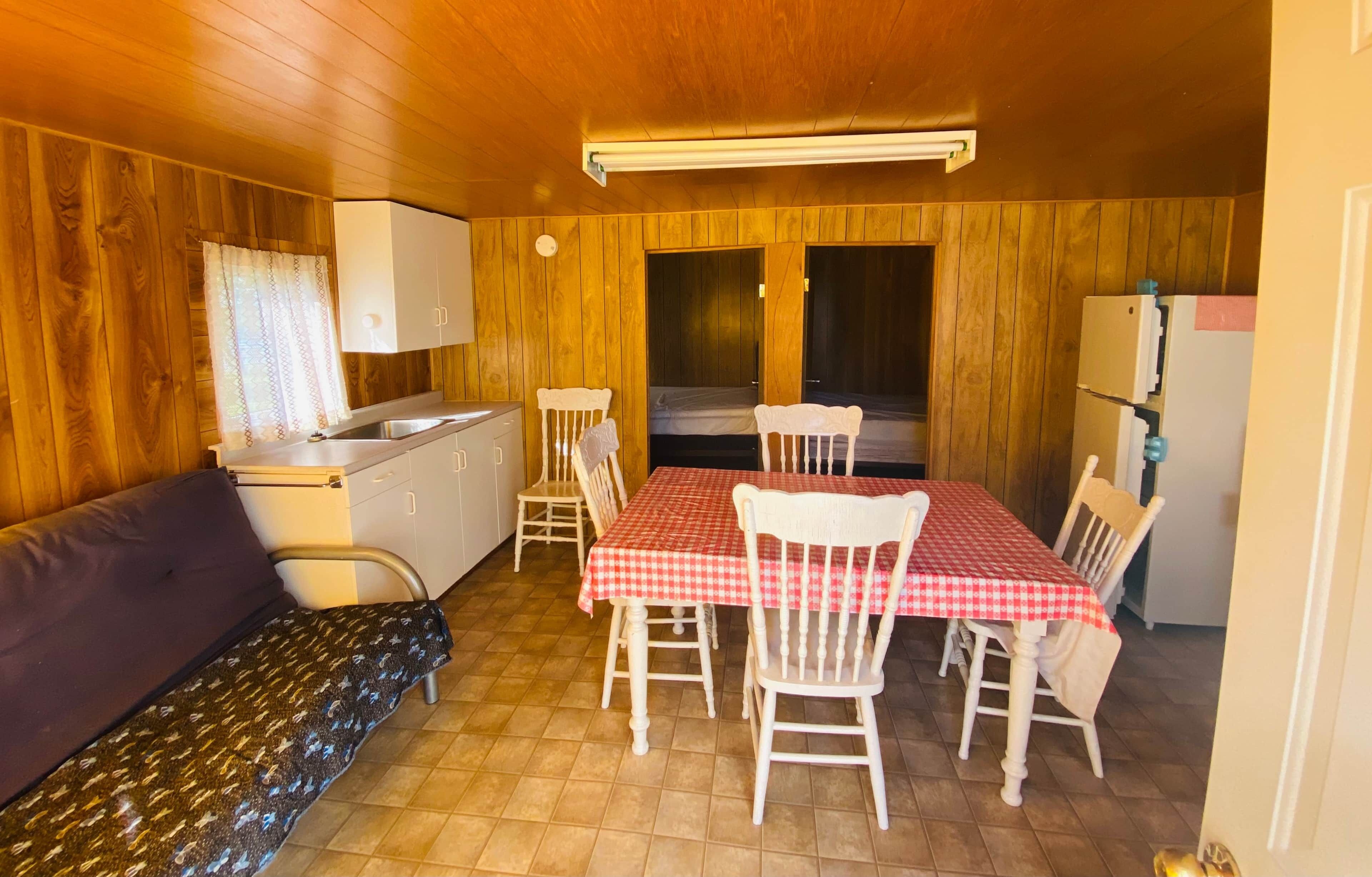 A compact room with a kitchenette, a dining table with chairs, a sofa, and a window.