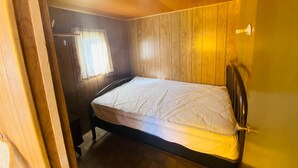 A wooden-paneled room with a single bed, a window with curtains, and a door.