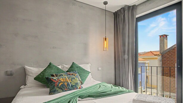 Ein Schlafzimmer mit einem Bett, Kissen, einer Hängeleuchte und Blick auf ein Gebäude durch ein Fenster.