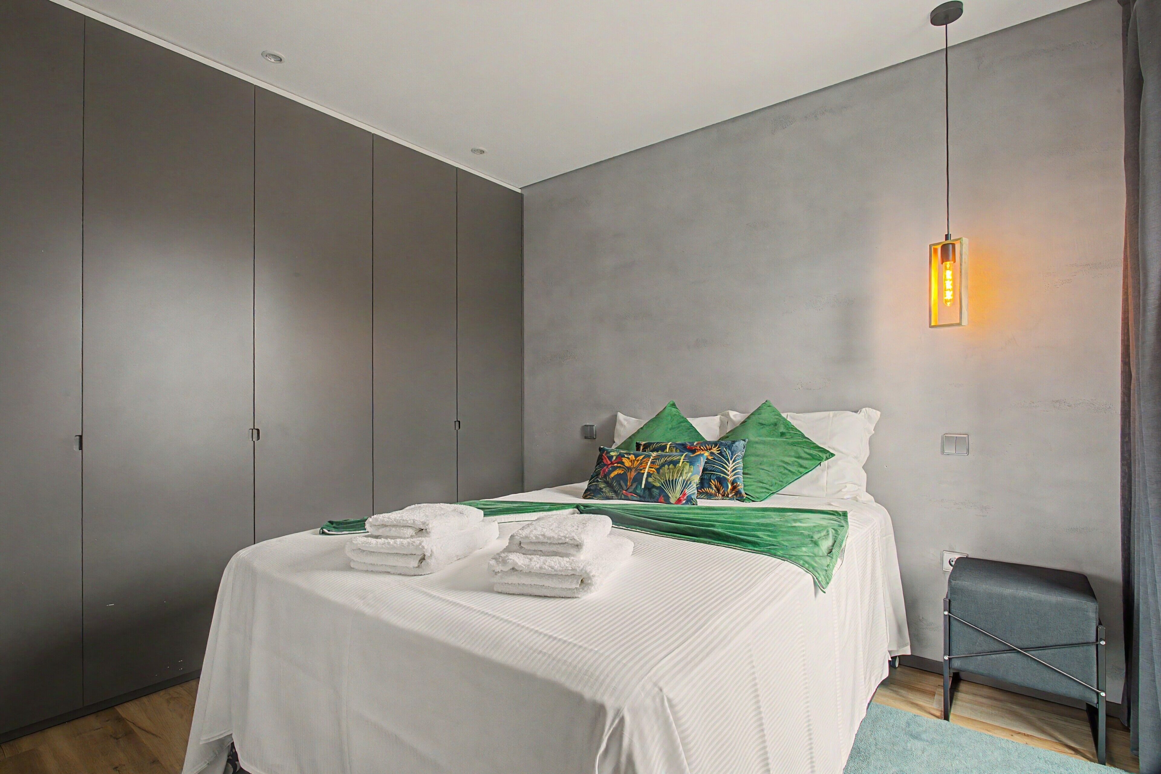 Un dormitorio moderno con cama, almohadas, una mesita de noche y una lámpara colgante.