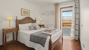 Une chambre à coucher avec un lit en bois, deux tables de chevet avec des lampes, un radiateur et une vue sur un balcon extérieur.