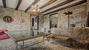 Une pièce au sol en pierre, avec une table de ping-pong, une chaise rouge et un lustre.