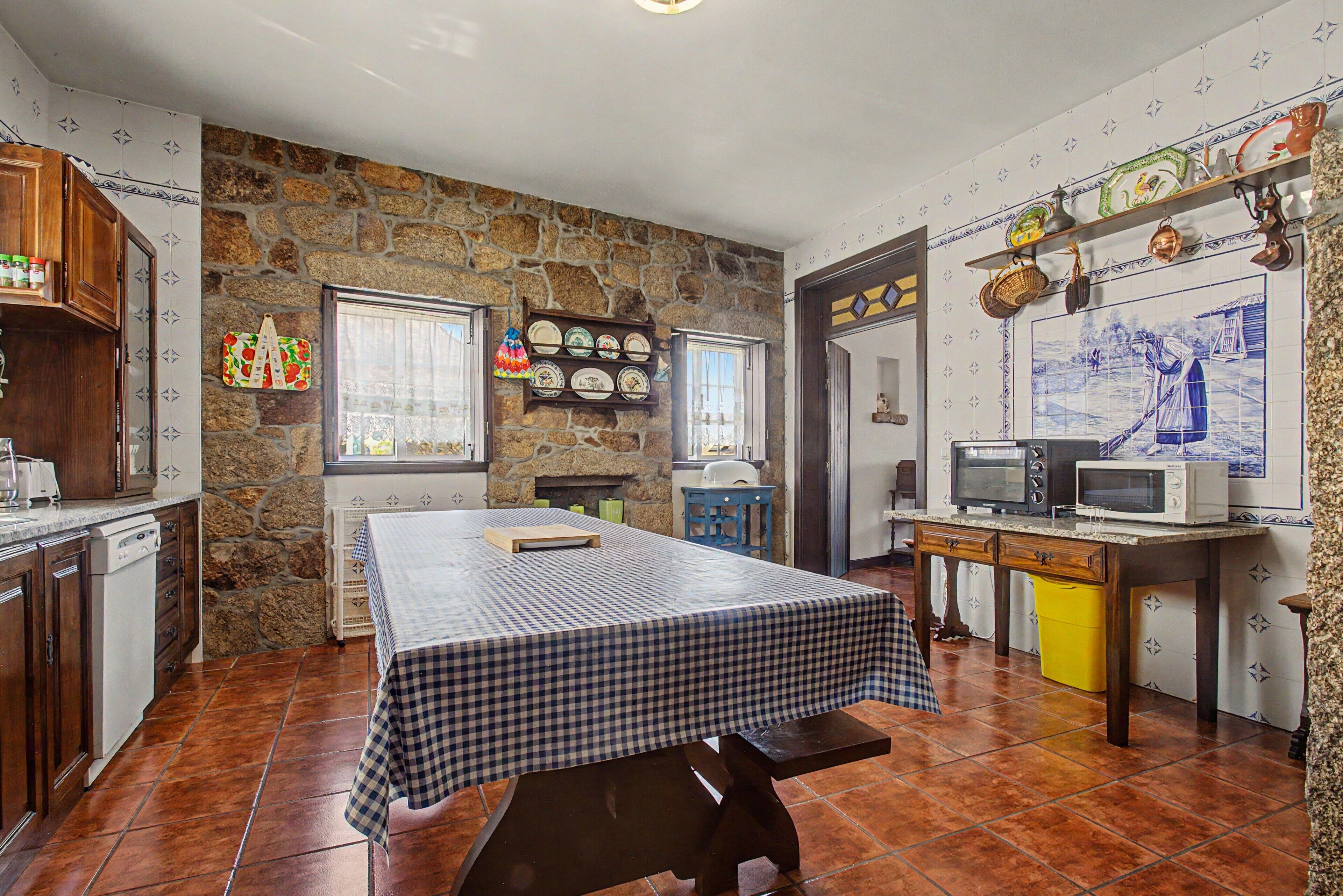 Una cocina con pared de piedra, una mesa a cuadros y suelo de baldosas.