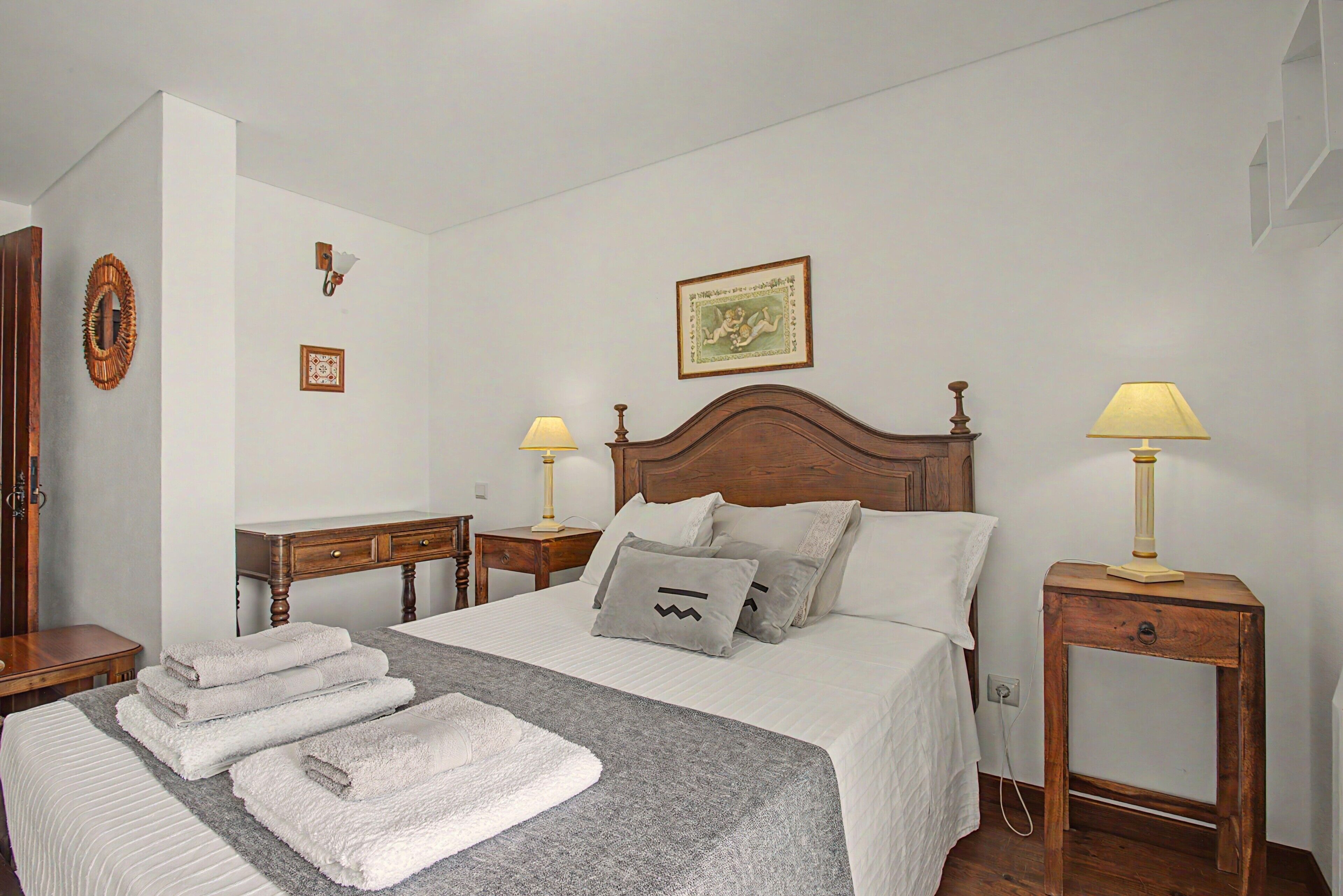 Una cama bien hecha con toallas, un cabecero de madera, lámparas de noche y un cuadro enmarcado en la pared.