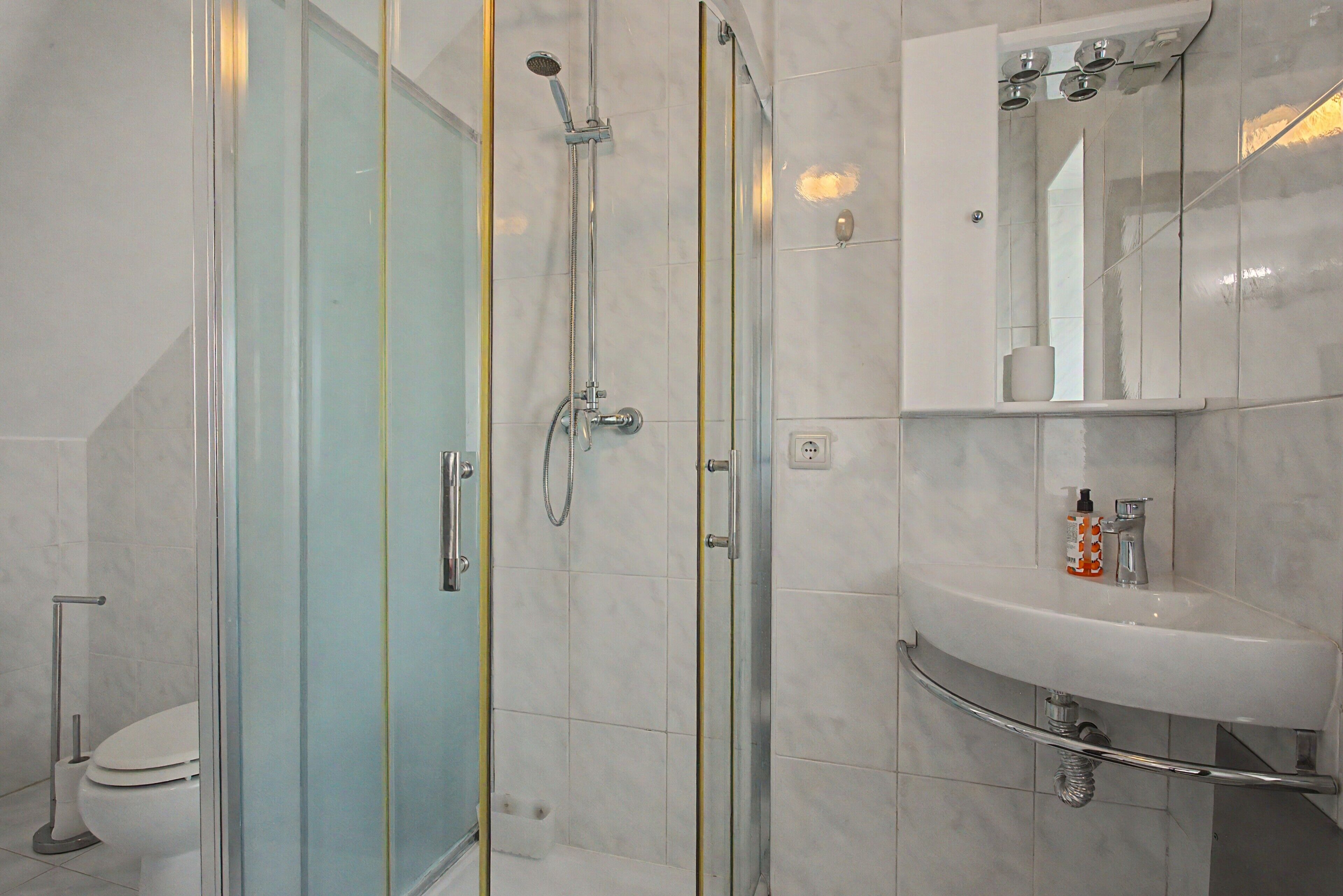 Un baño con ducha de vidrio, un lavamanos blanco y un espejo sobre él.