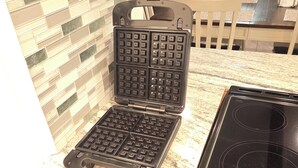 Una cocina con una plancha para gofres, estufa y salpicadero de azulejos.