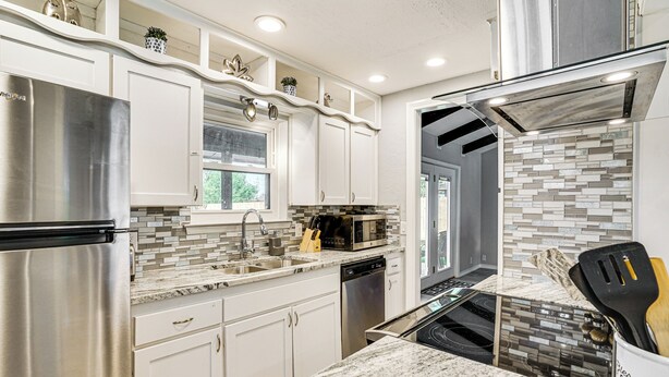 Una cocina moderna con armarios blancos, electrodomésticos de acero inoxidable y salpicadero de azulejos.