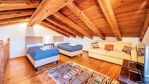 Een gezellig zolderkamer met een schuin houten plafond, twee bedden, een sofa en een televisie.