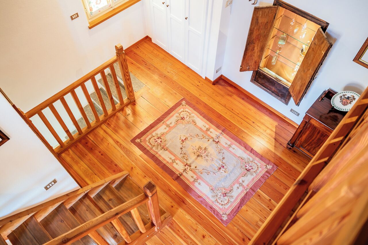 A wooden staircase with a handrail, a wooden floor, and a patterned rug.