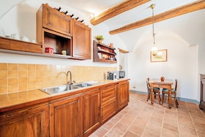 Une cuisine avec des meubles en bois, un évier à deux bacs et un coin repas comprenant une table et des chaises.