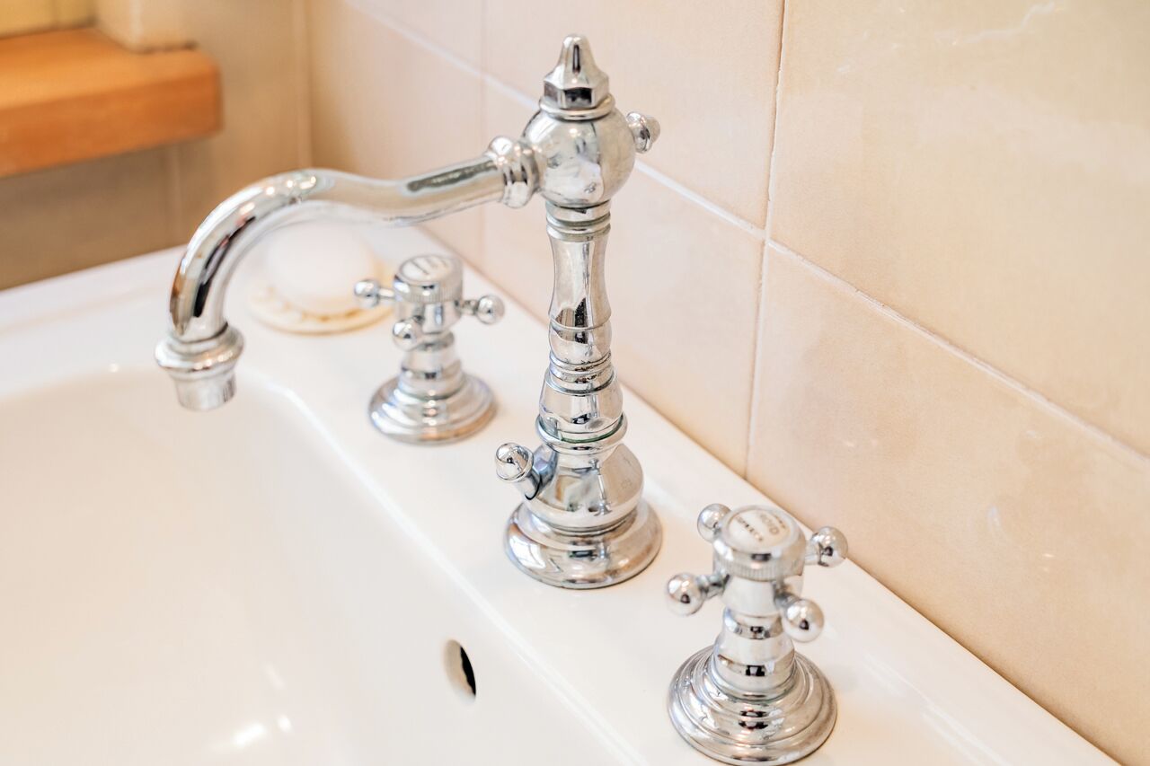 Un baño con una bañera blanca, tres grifos cromados y paredes cubiertas de azulejos color beige.