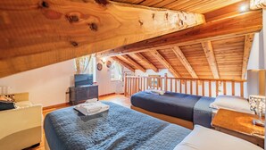 Een gezellig zolderkamer met twee bedden, houten balken, een klein bureau en een televisie.