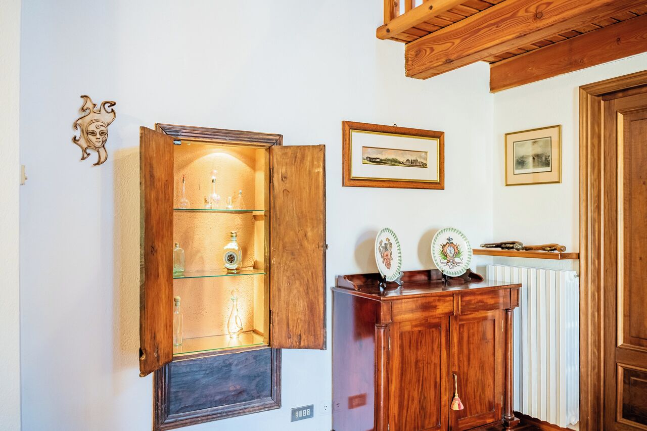 A wooden cabinet with glass shelves displaying bottles, a framed picture on the wall, and a radiator.