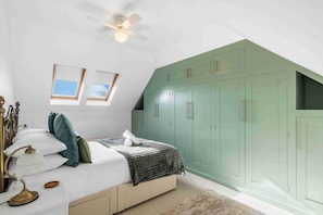 Une chambre à coucher avec un lit, un ventilateur de plafond, un puits de lumière et des armoires vertes.