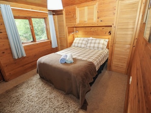 A wooden cabin bedroom with a bed, curtains, and a window.