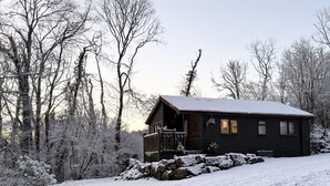 A log cabin with a porch, surrounded by snow-covered trees and a clear sky. - Ash Lodge (Llanelli)