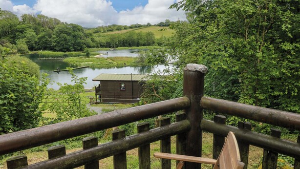 A wooden deck with a bench and a small cabin overlooking a lake. - Ash Lodge (Llanelli)