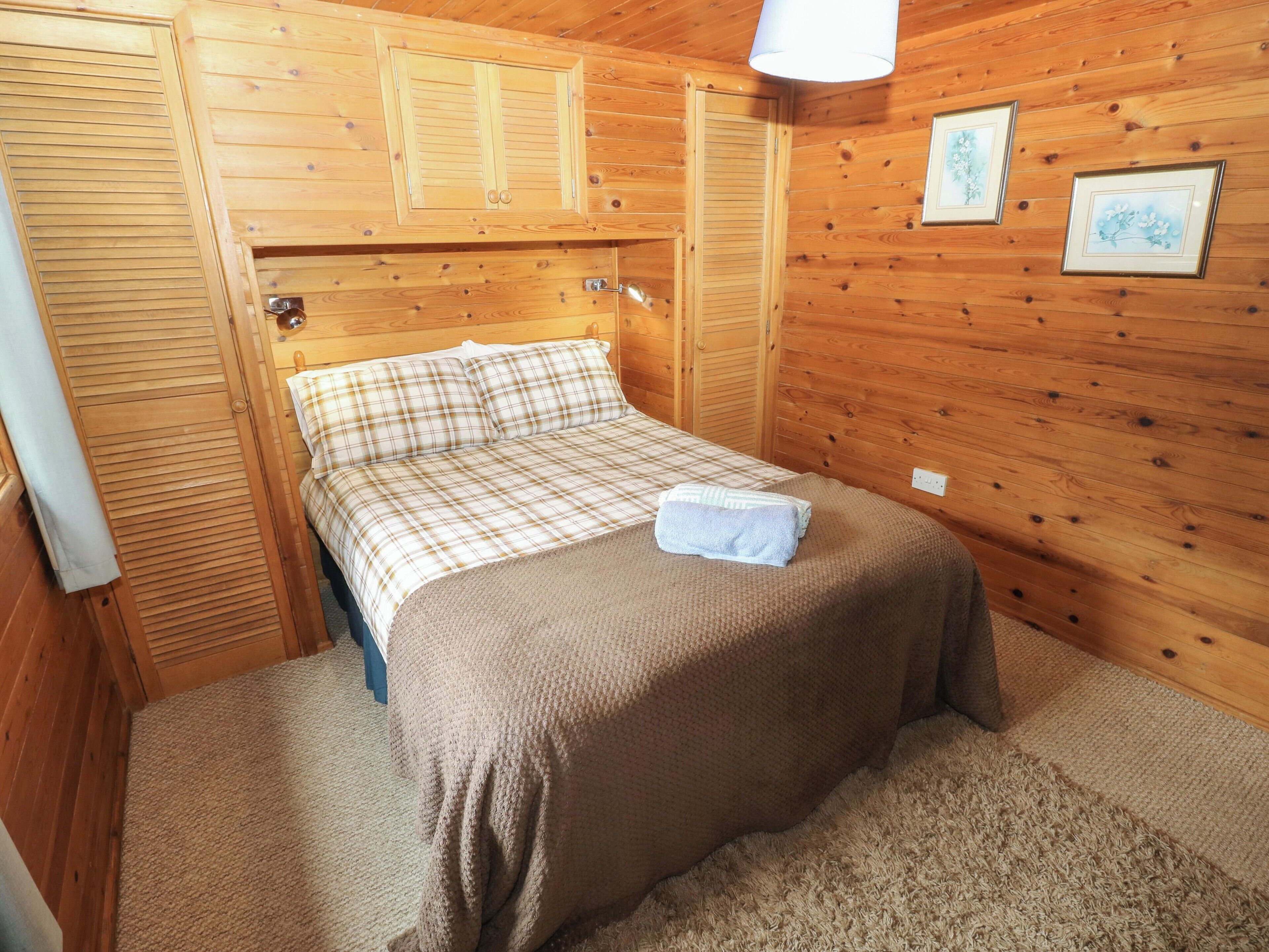 Een houten kamer met een bed, een houten kledingkast en een ingelijst schilderij aan de muur.