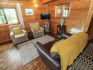 A cozy cabin interior with wooden walls, a sofa, two striped armchairs, a television, and a fireplace.